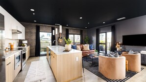 A modern kitchen with a central island, a dining area with a sofa and chairs, and a large window offering a city view.