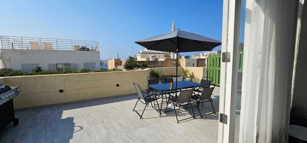 An outdoor patio with a table and chairs, a grill, and a large umbrella. - Valletta Penthouse Cathedral view Terrace (Valletta)