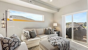 Un salon moderne avec un canapé, un pouf et une grande fenêtre donnant sur un chantier de construction.