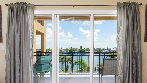 A balcony with a view of a lake and buildings, featuring a sliding glass door and grey curtains.
