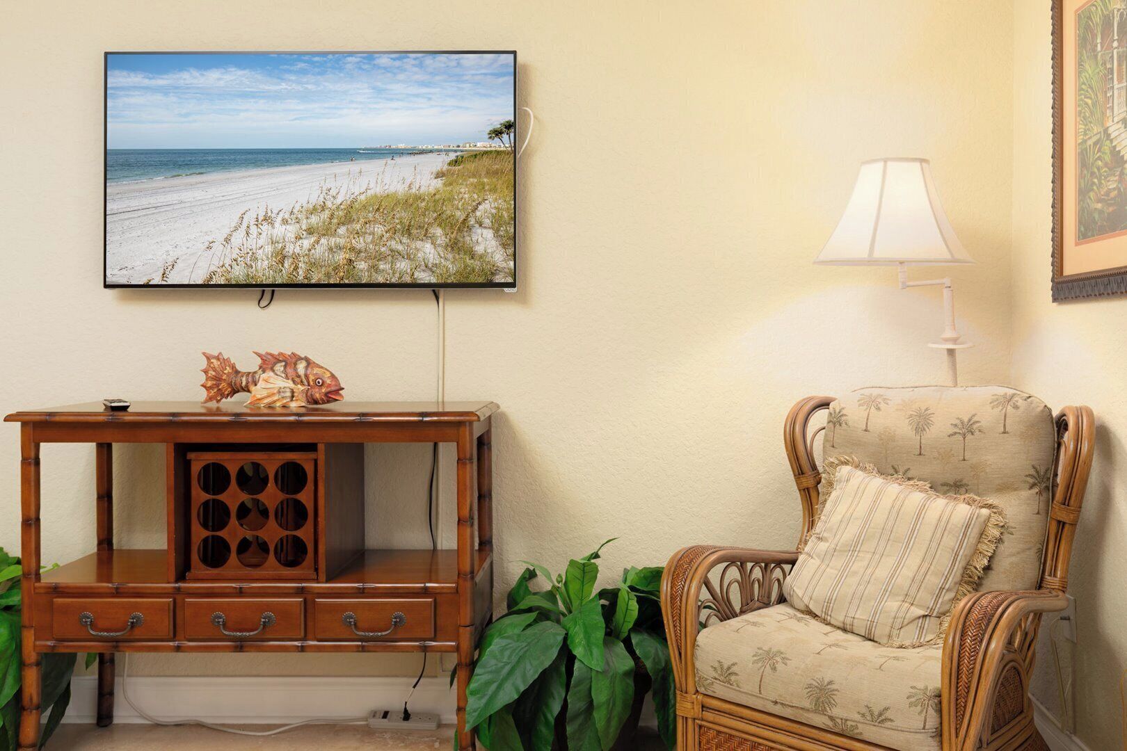 Un salón con vista al mar, un mueble de entretenimiento de madera, un sillón de mimbre y una lámpara blanca.