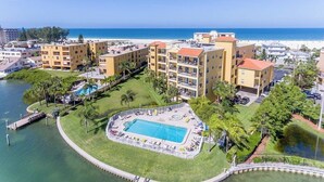 A resort with a central pool, multiple buildings, and a beach view.