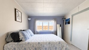 A bedroom with a bed, a window, a door, and a wall-mounted lamp.