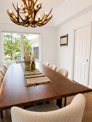 A long dining table with chairs, a chandelier, and a view of the outdoors. - Luxury Mountain-View Retreat | near Garden of the Gods | Hot Tub | Game Room (Colorado Springs)