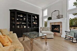 Ein Wohnzimmer mit Kamin, einem großen schwarzen Bücherregal und einem Glastisch.