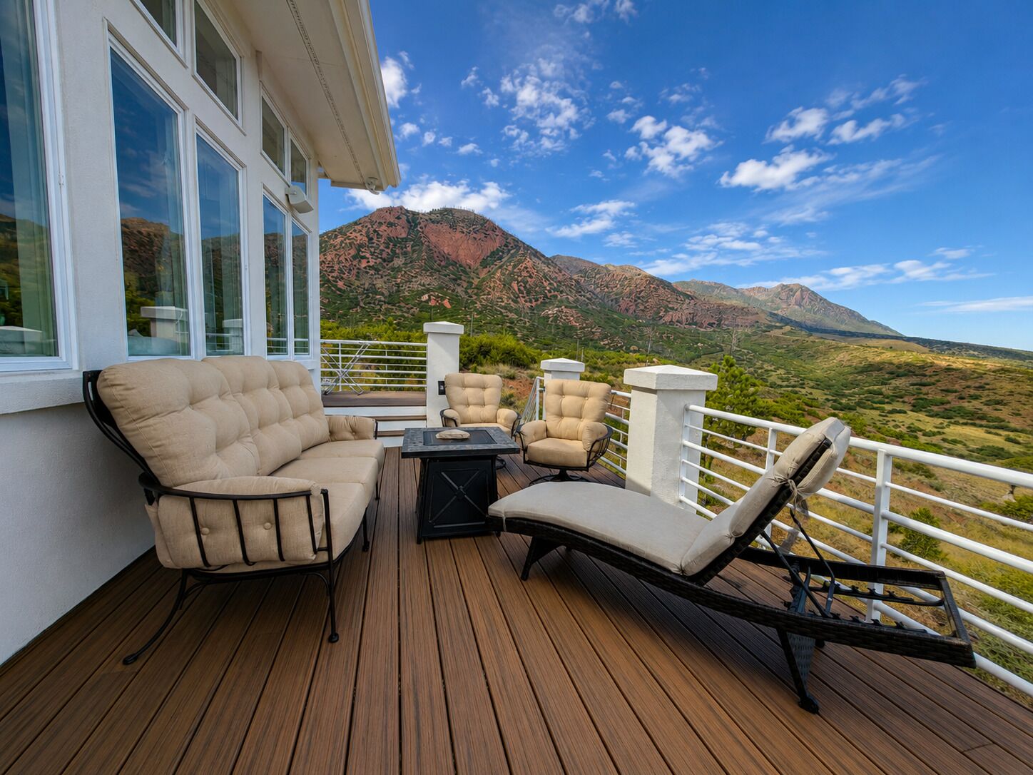 A deck with outdoor furniture, a view of mountains, and a white railing.