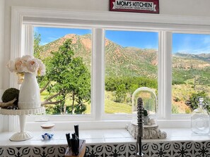 A kitchen with a view of a mountainous landscape through a large window. - Luxury Mountain-View Retreat | near Garden of the Gods | Hot Tub | Game Room (Colorado Springs)