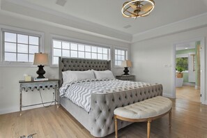 A bedroom with a large bed, two bedside tables, a bench, and a chandelier.