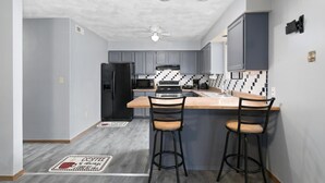 A modern kitchen with grey cabinets, a black refrigerator, a microwave, and a coffee bar with stools. - Touch of Class  3-bedroom townhome in Belleville King Bedroom. (Belleville)