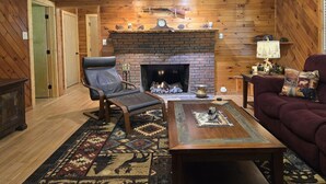 Un salon chaleureux avec une cheminée, un fauteuil en cuir, une table basse en bois et un tapis à motifs.