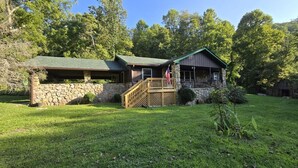 Un chalet rustique avec une façade en pierre, une terrasse en bois et un drapeau.