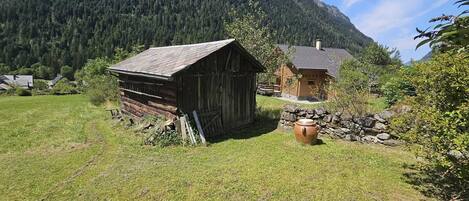 A rustic wooden cabin with a stone wall and a large clay pot in front.