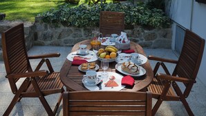 Une table ronde en bois, mise pour un repas, avec des chaises, des assiettes, des tasses et un pichet de jus d’orange.