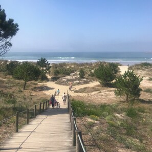 A wooden boardwalk leading to a beach with dunes and sparse vegetation.