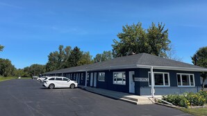 A row of single-story buildings with a dark blue exterior, a covered parking area, and a clear blue sky. - East Court Motel (Sarnia)