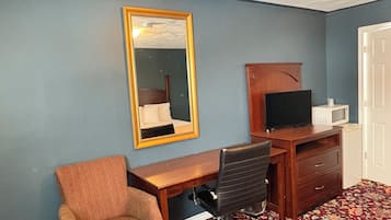 Una habitación con un escritorio de madera, una silla de oficina negra, un televisor sobre un mueble de madera y una puerta blanca.