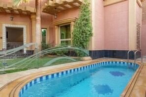 A swimming pool with a curved edge, surrounded by a tiled deck and a palm tree.