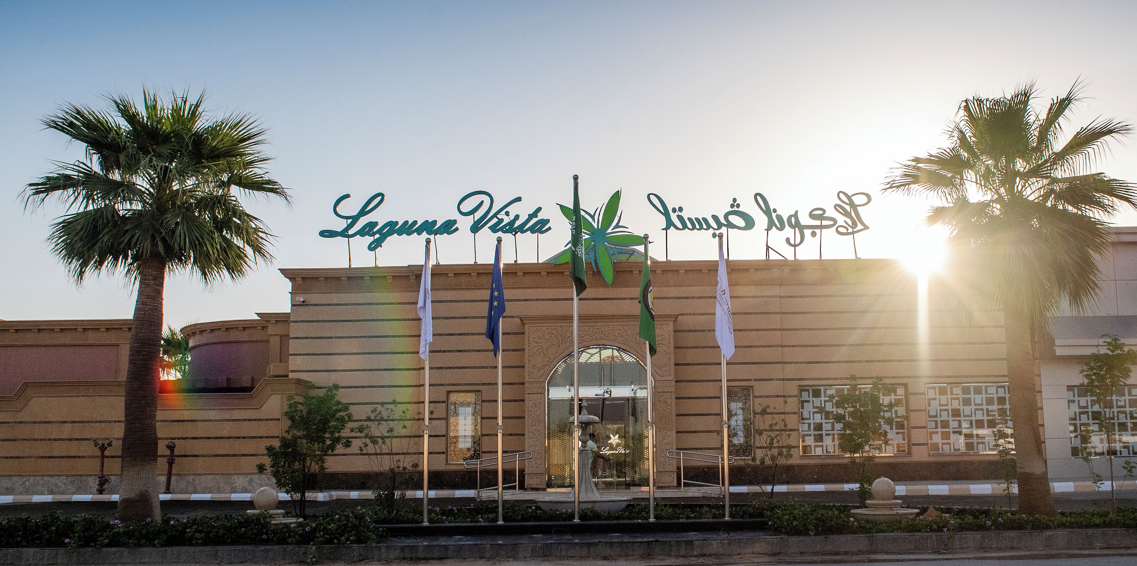 Entrada de hotel con un cartel que dice "Laguna Vista" y varias banderas.