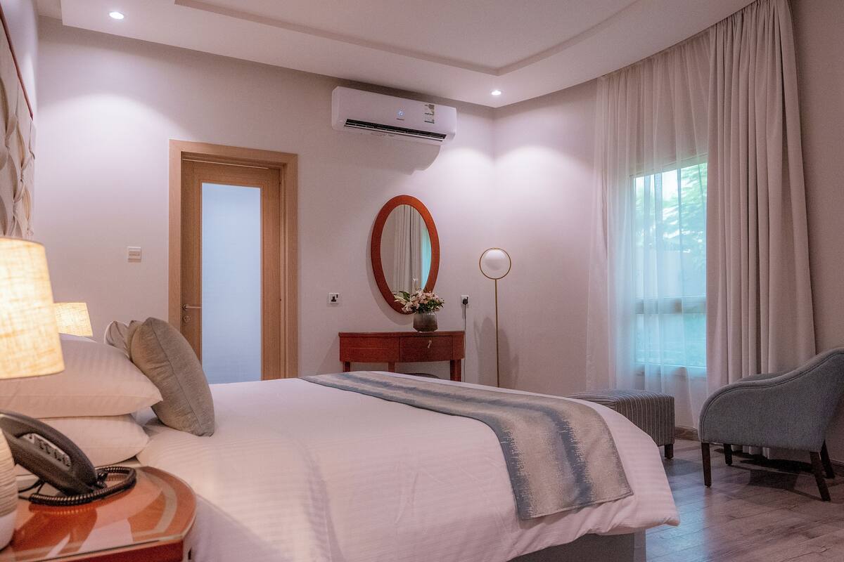 Ein Hotelzimmer mit Bett, Nachttisch, Lampe, Spiegel und einem Sessel.