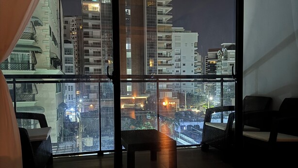 Une chambre d’hôtel moderne dotée d’un grand balcon offrant une vue sur le paysage urbain la nuit.