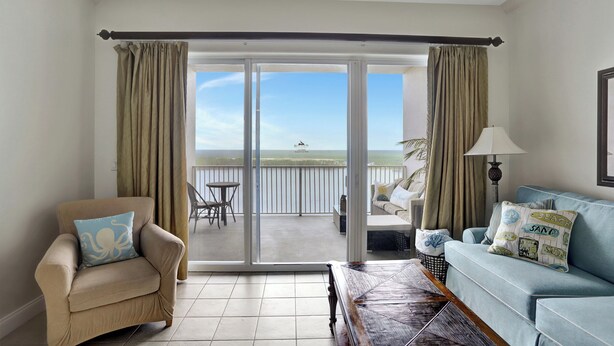 Ein Zimmer mit einem beigen Sessel, einem blauen Sofa und Meerblick durch eine Schiebeglastür.