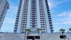 Ein Hochhaus-Hotel mit mehreren Balkonen, einem zentralen Eingang und Palmen im Vordergrund.