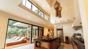 Una cocina moderna con una isla central, un comedor con puerta de vidrio que da a un patio, y un ventanal que proporciona luz natural.