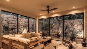 Una sala de estar moderna con una pared de piedra, ventanas amplias y un ventilador de techo.