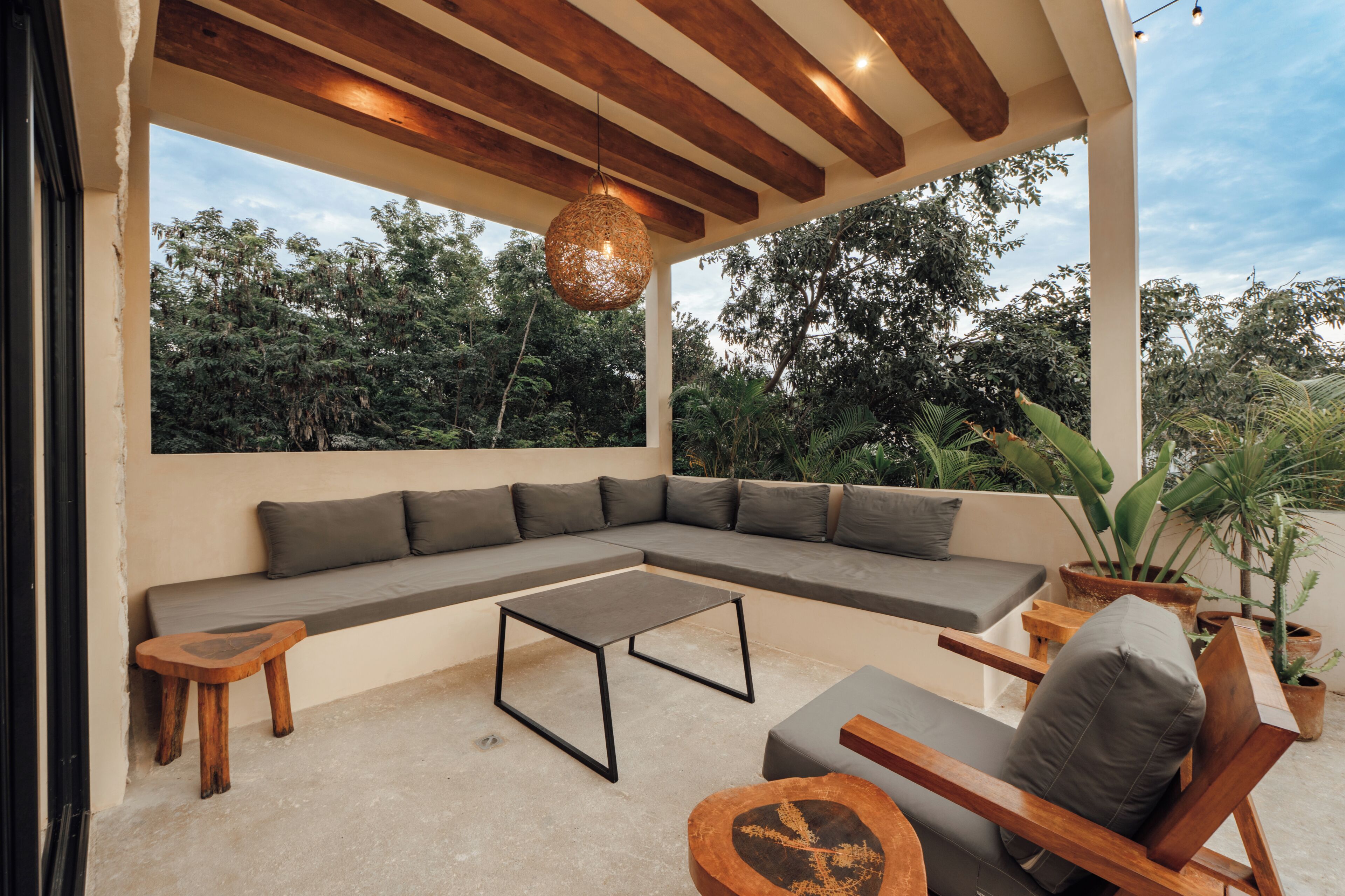A covered outdoor seating area with a sofa, a table, and chairs, surrounded by potted plants.