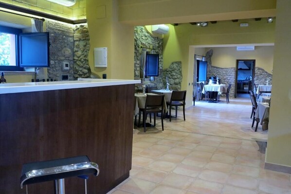 A restaurant with a stone wall backdrop, a counter with a bar stool, and multiple tables with chairs. - Hotel Can Panyella (Gelida)