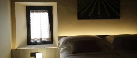 Un dormitorio con cama, una mesita de noche con lámpara, una ventana con cortinas y una obra de arte colgada en la pared.
