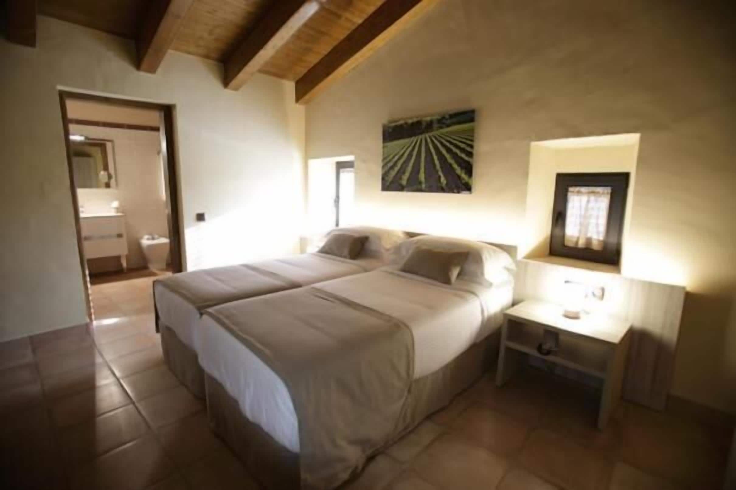 A bedroom with a large bed, a bedside table, a wall-mounted lamp, and a framed picture.