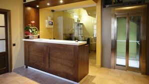 Un área de recepción con mostrador de madera, una planta pequeña y una puerta de vidrio que da a una cocina.
