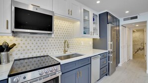Una cocina moderna con armarios blancos, una estufa de acero inoxidable, un microondas integrado y un refrigerador.
