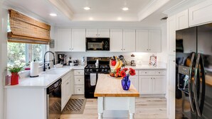 Une cuisine moderne avec des meubles blancs, un plan de travail en bois, une cuisinière noire et un réfrigérateur en acier inoxydable.