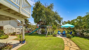 Un jardin avec une aire de jeux, un chemin en pierre et un espace salon extérieur.