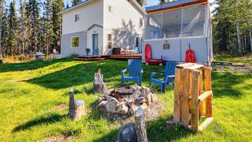 Relax on the deck with a fire pit, surrounded by lush greenery and a forested backdrop.