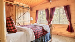 A wooden cabin bedroom with a bed, curtains, and a window.