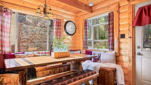 A cozy cabin interior with a wooden dining table, stone wall, and a clock on the wall.