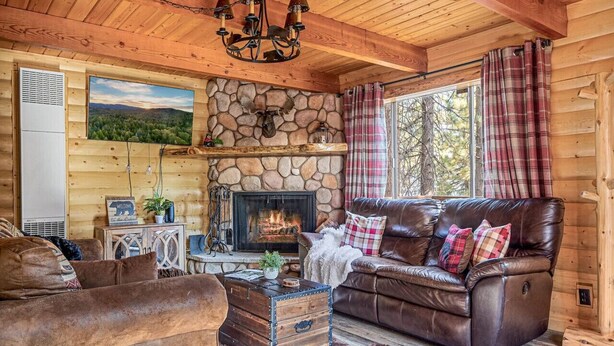 A cozy cabin interior with a stone fireplace, leather sofa, and a rustic wooden ceiling.