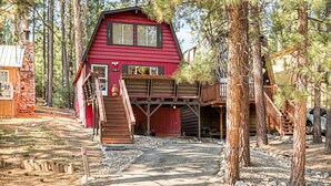 A red cabin with a wooden deck and stairs leading to a garage.