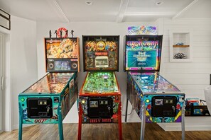 Three pinball machines in a room with white walls and a wooden floor.