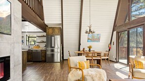 Amplia sala de estar con chimenea, piso de madera, una mesa de comedor con sillas y una cocina con electrodomésticos modernos.
