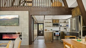 Amplia sala de estar con chimenea, mesa de comedor y cocina equipada con electrodomésticos modernos.