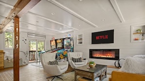 Una sala de estar con chimenea, paredes blancas y un televisor montado mostrando 'NETFLIX'.