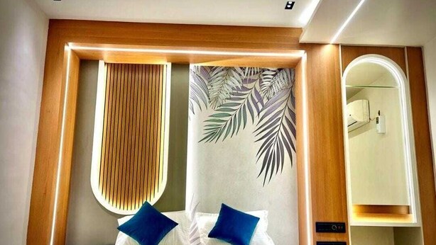 Camera d'albergo moderna con un letto grande, una testiera in legno, un muro decorato con un motivo a foglia e una libreria a incasso.