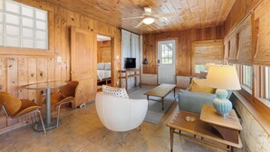 A cozy cabin interior with wooden walls, a ceiling fan, a TV, a dining area, and a seating area with a lamp. - Waterlily Serenity | 2 Bedroom | Creekside (Wimberley)