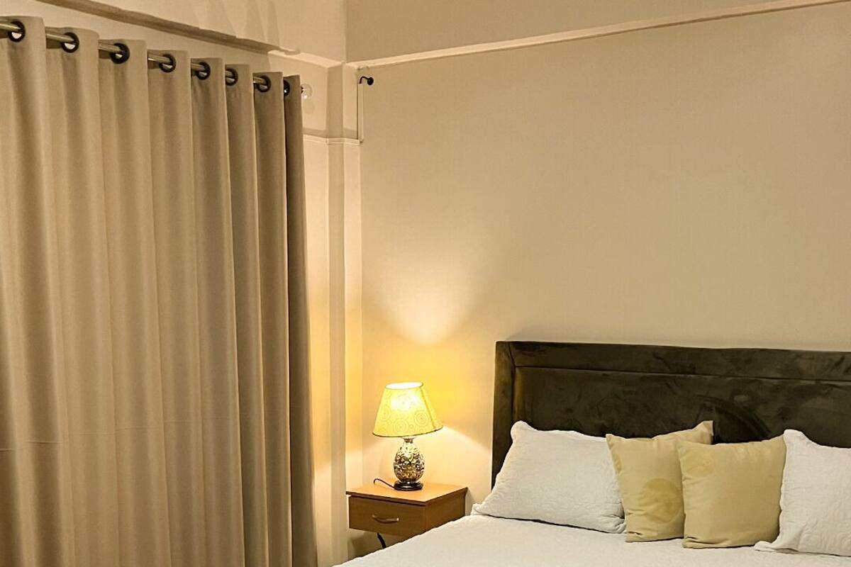 A neatly made bed with a white quilt, a bedside lamp, and a dark headboard.