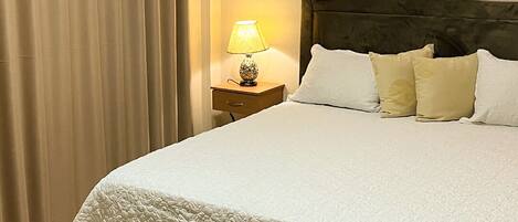 A neatly made bed with a white quilt, a bedside lamp, and a dark headboard.
