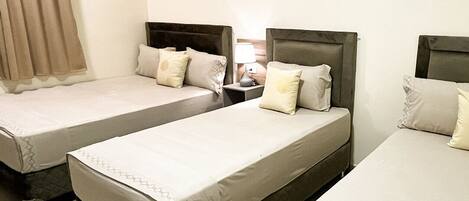 A hotel room with two single beds, a nightstand with a lamp, and an air conditioning unit on the wall.